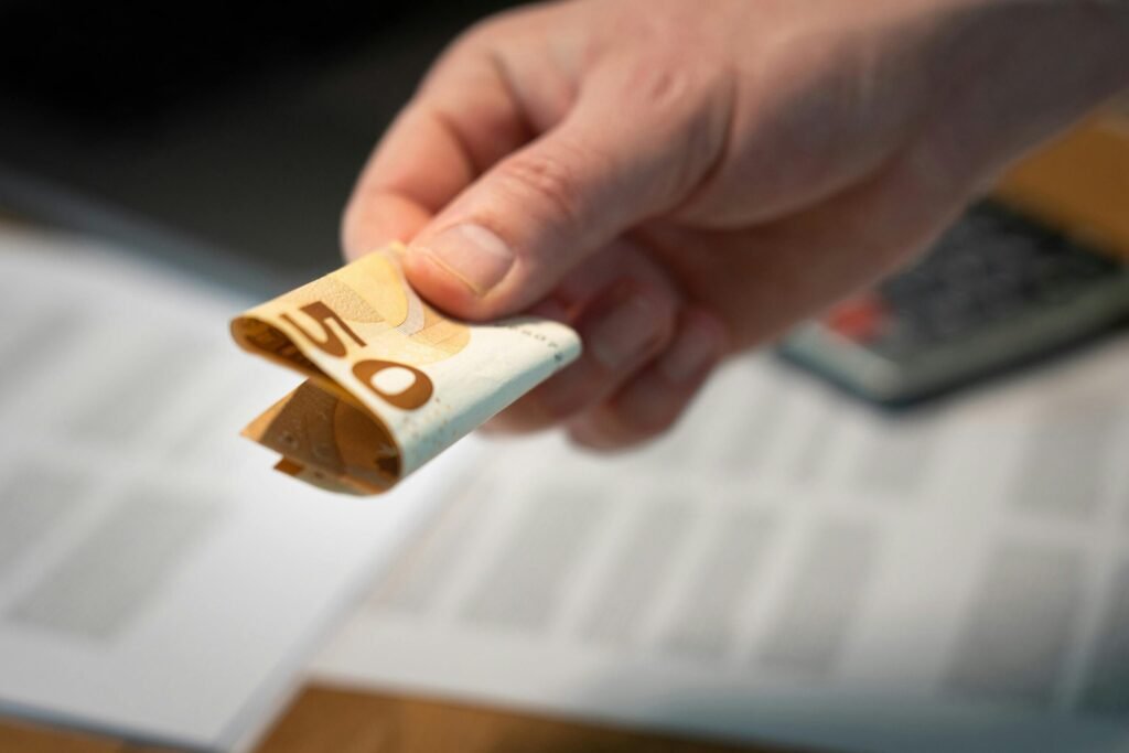 A detailed image of a hand holding a folded 50 euro banknote, with documents in the background.