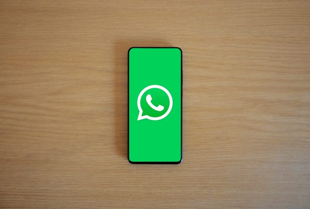 Top view of smartphone displaying WhatsApp logo on a wooden background, representing technology and communication.