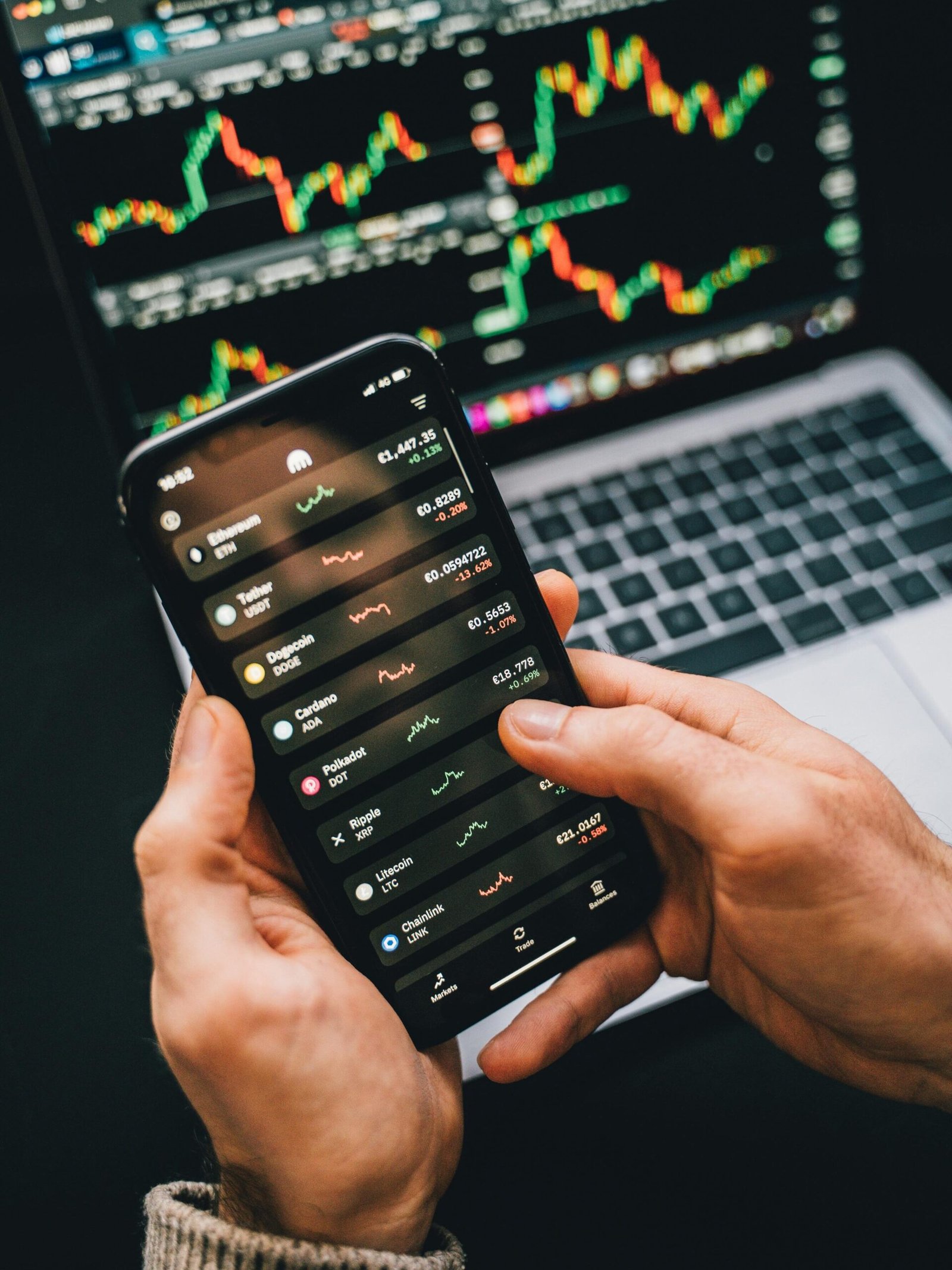 Hands holding smartphone with stock app, laptop displaying charts. Perfect for financial and technology themes.