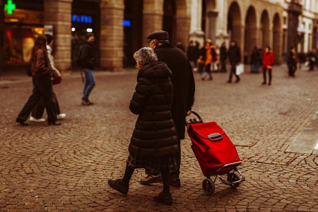 An elderly couple walking through the historic streets of Padova, Italy, with a red trolley bag.