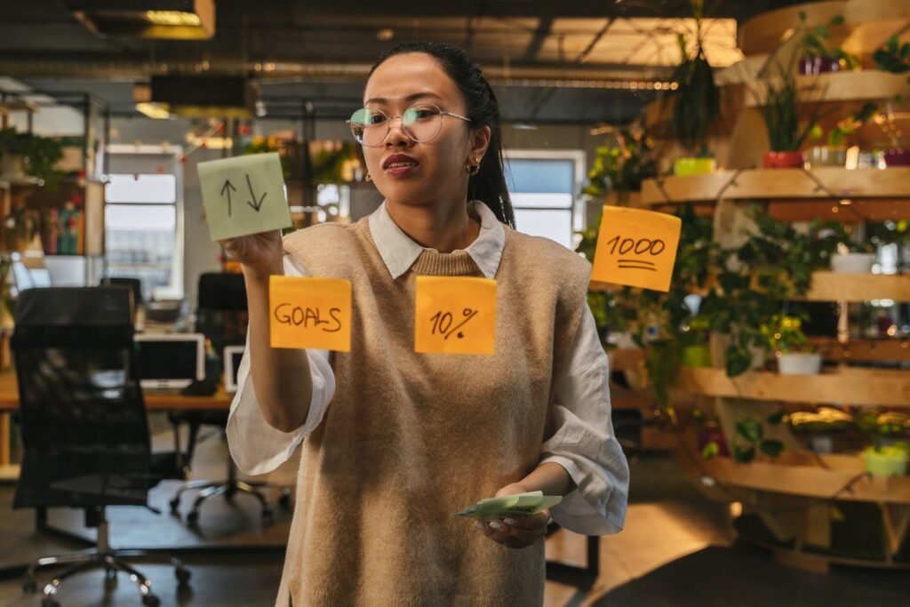 Asian woman organizing tasks on sticky notes at modern office workspace.